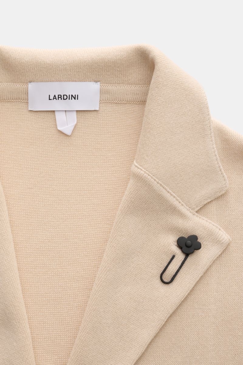 Lardini Strickblazer creme aus reiner Baumwolle mit feinem Strickbild, fallendem Revers und schwarzem Blüten-Anstecker, Nahaufnahme von oben.