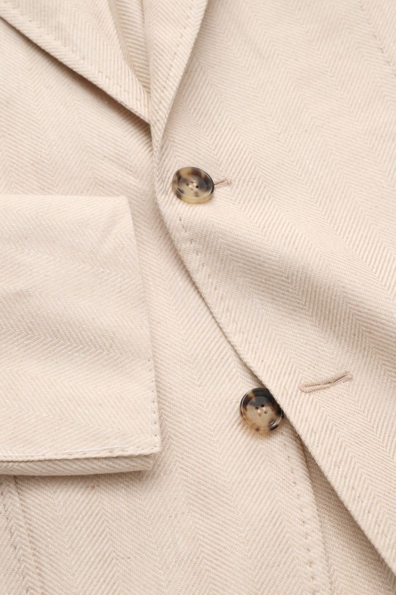 Close-up front detail of the Sipario Smart-casual jacket 'Ginza' sand patterned, showing tonal herringbone fabric, two buttons, step lapel, and classic breast pocket from an angled top perspective.

Description: Lightweight and stylish: The smart-casua