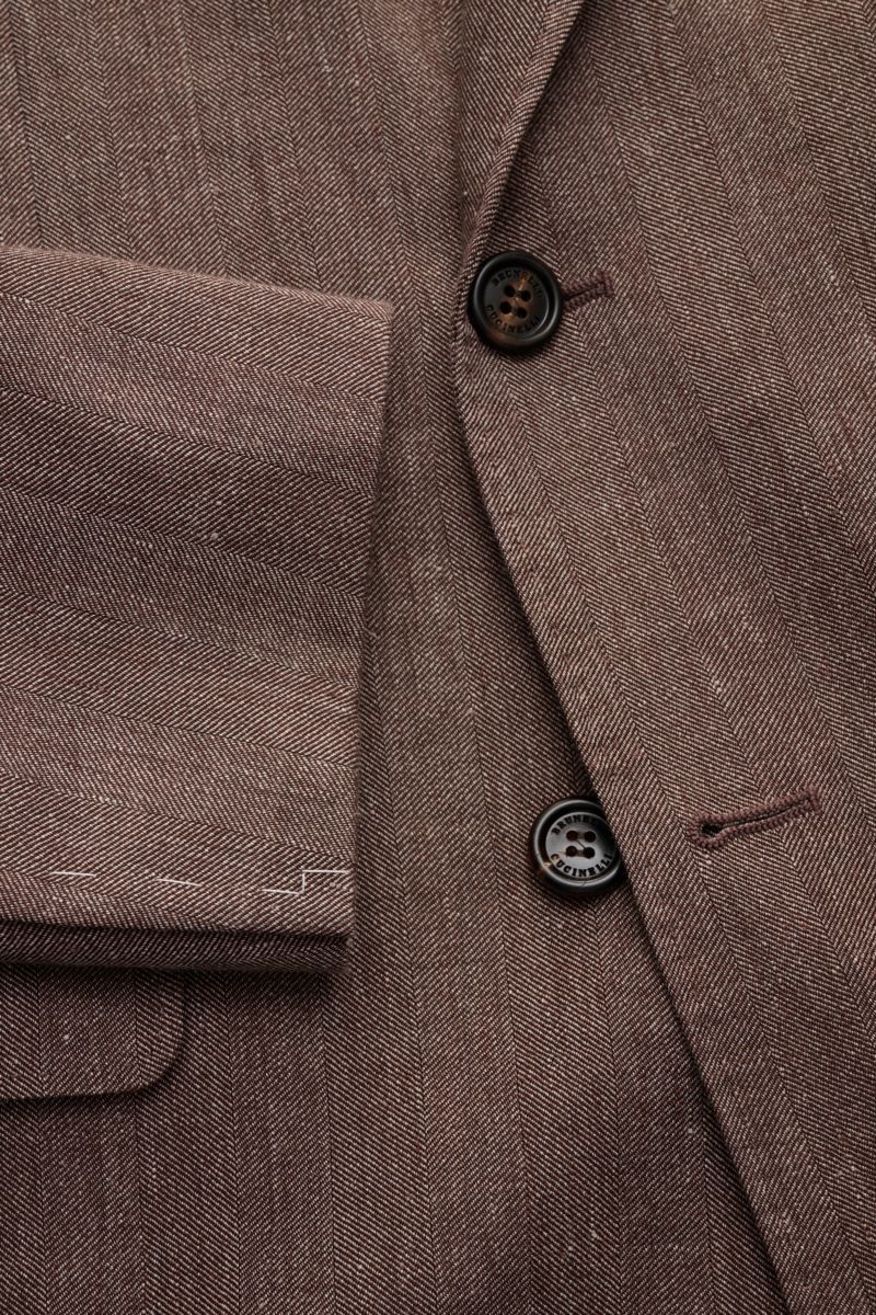 Close-up front view of the Brunello Cucinelli Sakko graubraun meliert showcasing its tonal herringbone pattern, soft linen-wool mix fabric, two-button closure with branded buttons, and detailed cuff stitching for an elegant business look.