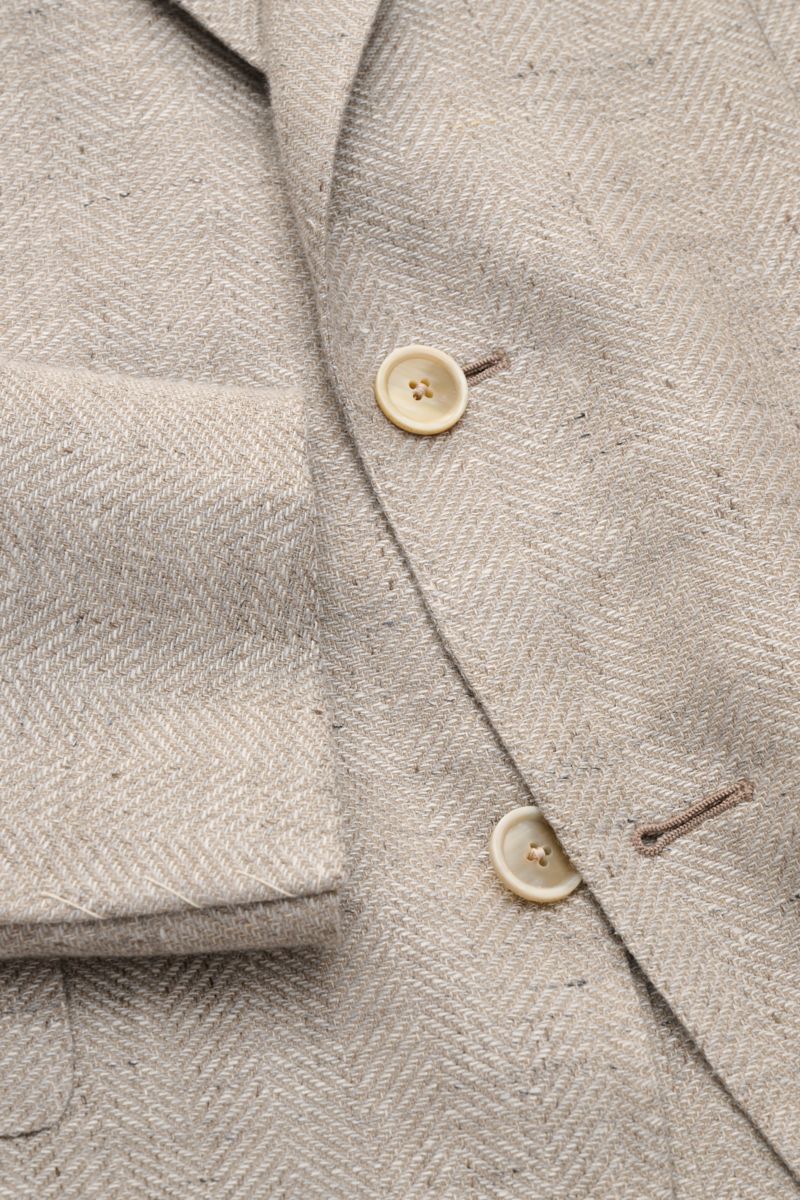 Close-up of Caruso Smart-casual jacket 'Aida' beige mottled showing herringbone texture, buttons, and sleeve cuff from a top-front angle.

In the smart-casual jacket 'Aida', CARUSO combines smart style with fabric in the natural materials linen and woo