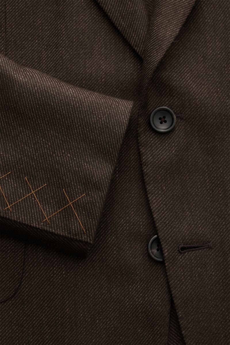 Nahaufnahme aus schräger Perspektive des dunkelbraunen Zegna Sakkos mit feinem Webmuster, zwei Knöpfen, fallendem Revers und weichem Griff.