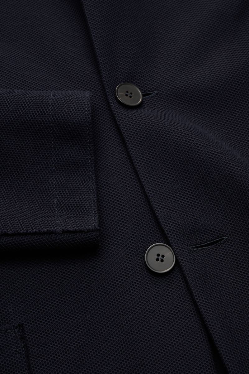 Harris Wharf London Knit blazer navy shown in close-up from a top-down angle, featuring pure cotton piqué, four buttons, patch hip pockets, and open edge finish, slim fit with a slim standing collar, unlined with two inside pockets. HARRIS WHARF LONDON