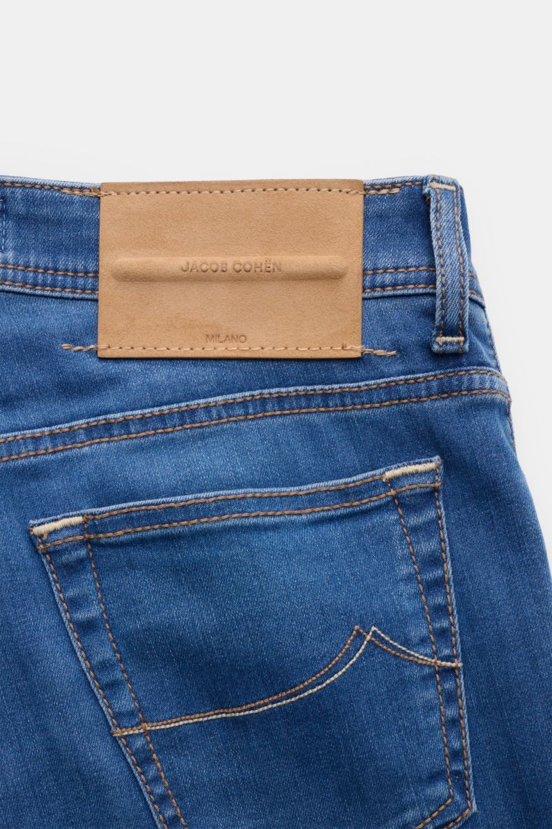 Close-up rear view of Jacob Cohen Jeans 'Bard' blau showing blue denim fabric, stitched back pocket, and tan leather patch with embossed logo. Modern luxury with a soft touch, slim fit, button fly, five-pocket style, coin pocket with initial, and detailed