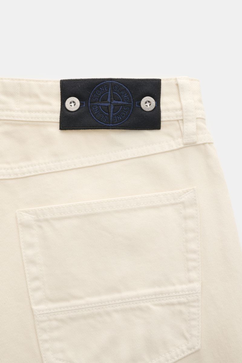 Detailaufnahme der Stone Island Jeans 'Light Bull Denim' creme von hinten mit typischem Kompass-Badge am Bund aus Baumwoll-Denim.