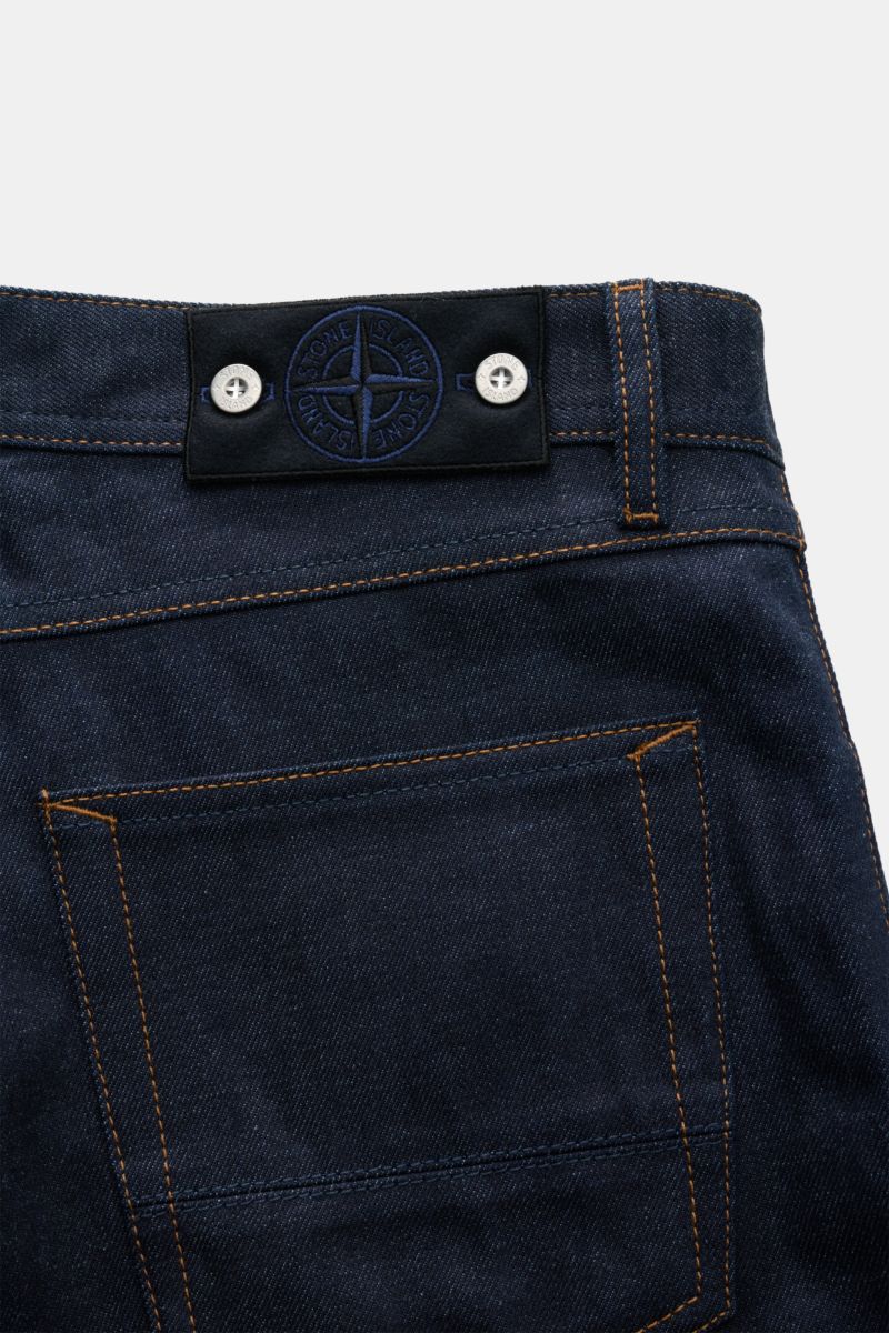 Back view close-up of Stone Island Jeans 'Selvedge Indigo Denim - Raw' navy, showing raw denim fabric, orange stitching, typical compass badge on waistband, and straight fit design.