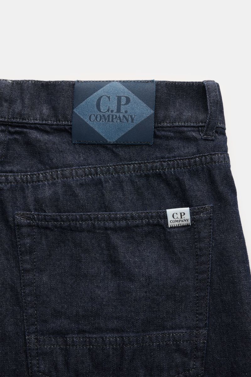 Close-up rear view of C.P. Company Jeans navy showing the waistband with leather patch, back pocket with logo tag, and dark navy denim fabric.