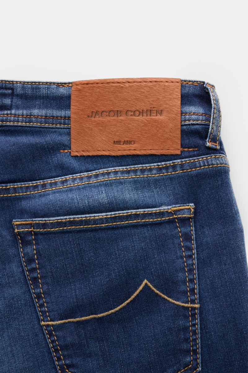 Close-up back view of Jacob Cohen Jeans 'Nick' blue showing denim made of cotton with elasticated fabric, soft feel, subtle used wash, slim fit, tapered cut, button fly, five-pocket style, coin pocket with initial, back pockets with stitching, and leather