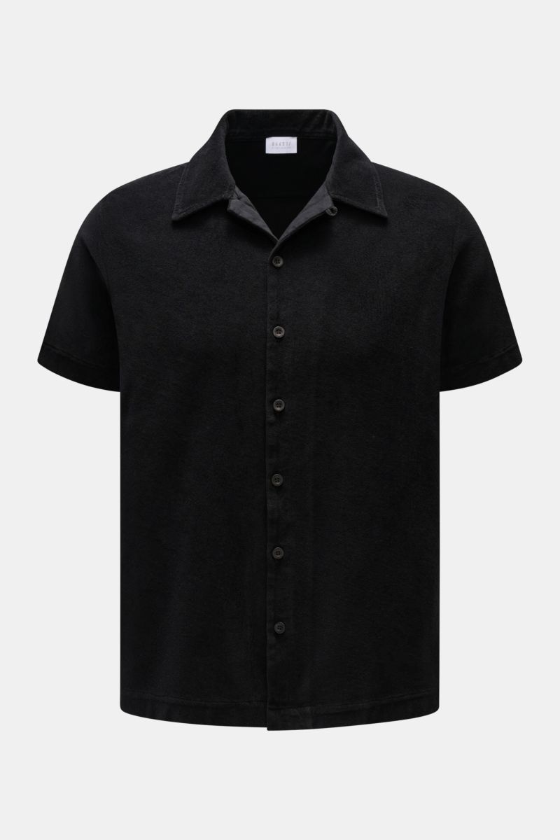 Front view of the 04651/ A trip in a bag Frottee-Kurzarmhemd 'Terry Cuba' schwarz, a black short-sleeve shirt made of soft cotton terry fabric with a regular fit, variable Cuban collar, French button placket, small side seam label, and short hem slits. Ur