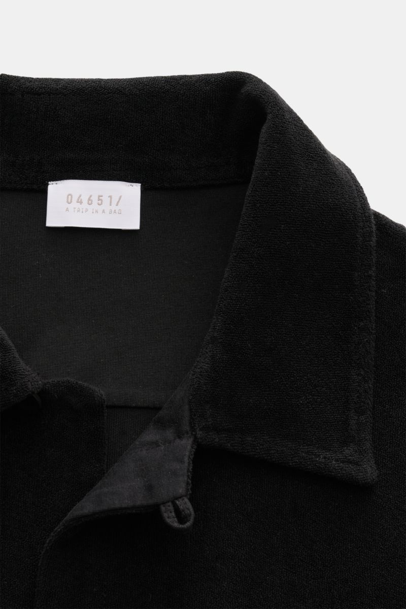 Close-up view of the collar and neckline of the 04651/ A trip in a bag Frottee-Kurzarmhemd 'Terry Cuba' schwarz, showing the soft cotton terry fabric and label. Urlaubsgefühl zum Anziehen: Das Kurzarmhemd 'Terry Cuba' von 04651/ A TRIP IN A BAG aus angene