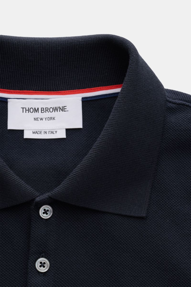 Nahaufnahme des Thom Browne Poloshirts navy von oben, mit klassischem Polokragen, fünf-Knopf-Leiste und markentypischem Streifen-Logo.