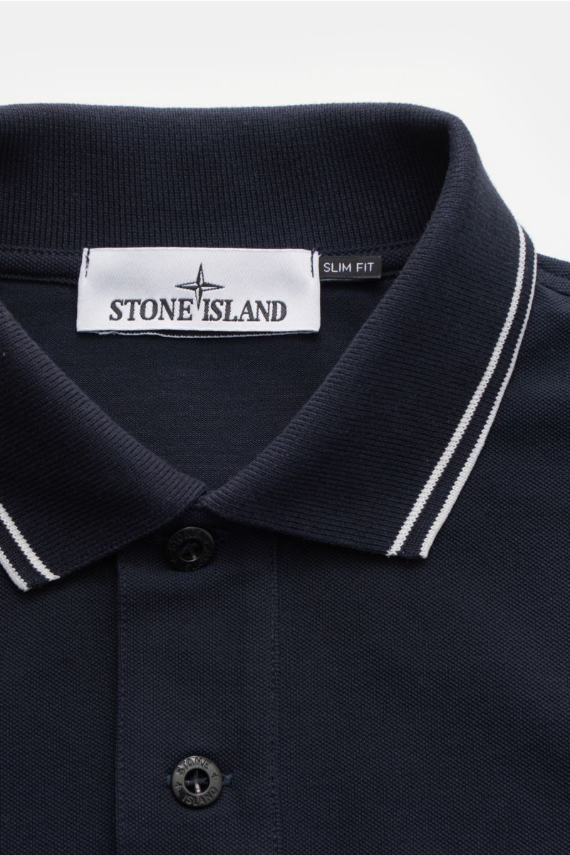 Stone Island Poloshirt navy shown from a close-up top-down perspective, featuring a slim fit piqué cotton fabric with soft texture, narrow white contrast stripes on the collar, typical polo collar, button placket with Stone Island-branded buttons, and ela