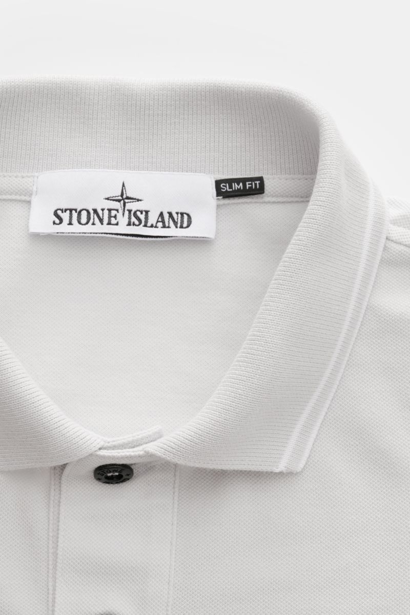 Nahaufnahme des Kragens und der Knopfleiste des Stone Island Poloshirt sand aus elastischer Baumwolle mit slim Fit und schmalen Kontraststreifen, fotografiert von oben.