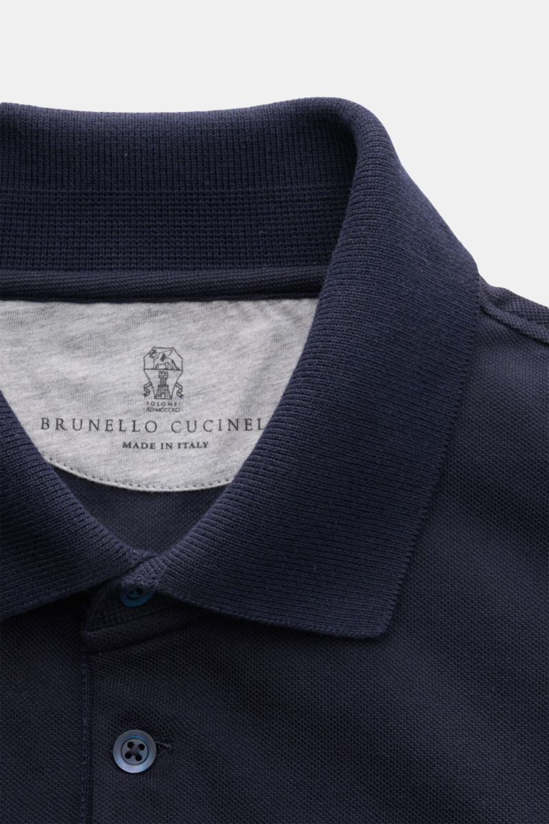Close-up front view of a navy blue Brunello Cucinelli Poloshirt graublau showing the classic piqué fabric, slim fit, tailored collar, three-button placket, ribbed cuffs with narrow contrast edge, and short side slits. Cleanes Essential erster Wahl: Liebha