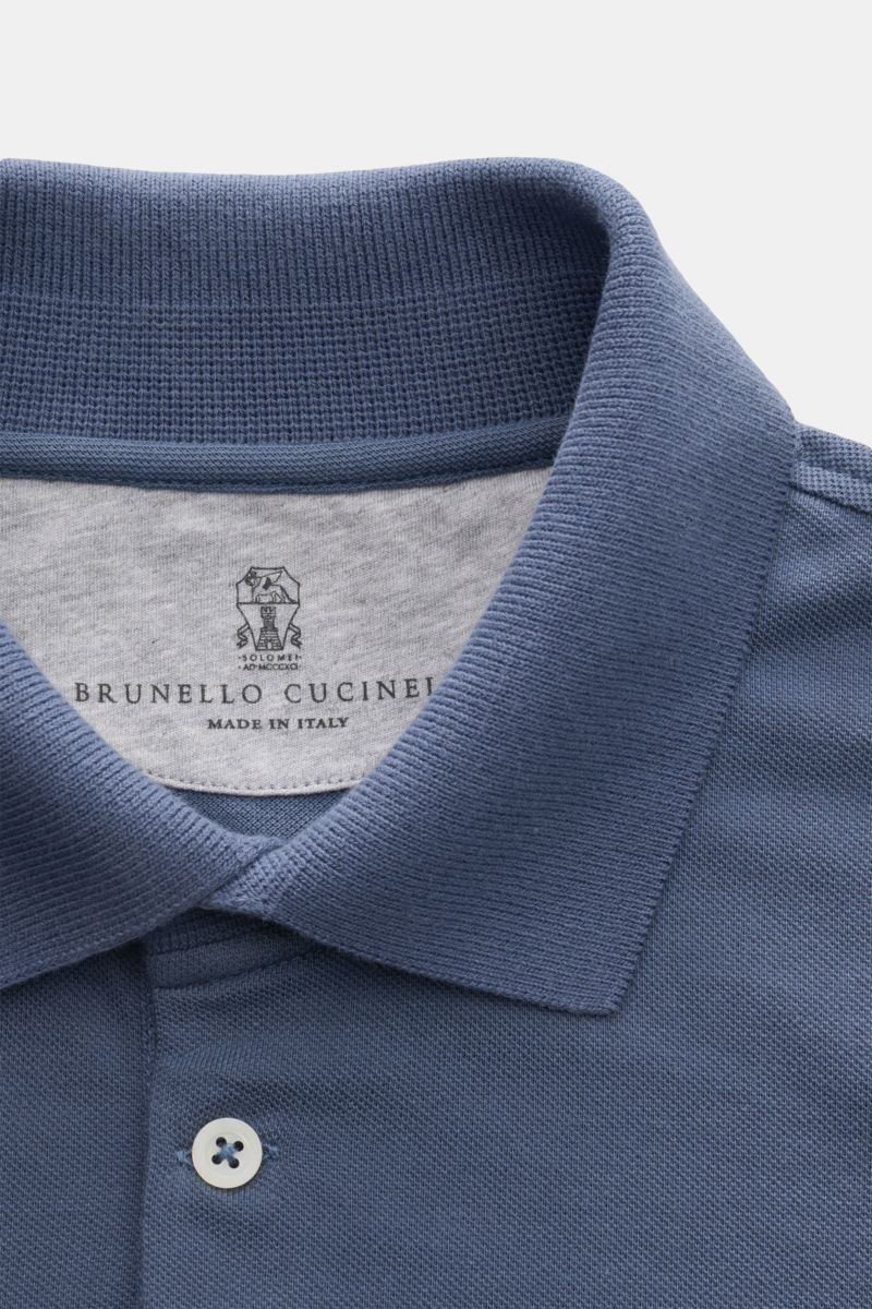 Close-up front view of a blue Brunello Cucinelli Poloshirt weiß showing the classic piqué fabric, slim fit, tailored collar, three-button placket, ribbed cuffs with contrast edge, and short hem slits. Cleanes Essential erster Wahl: Liebhaber der Luxusm