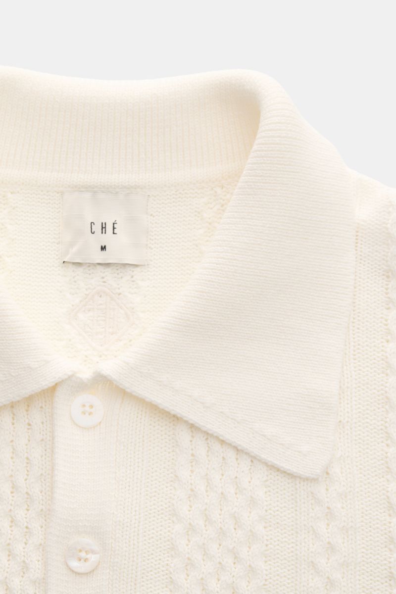 Close-up front view of the Ché Kurzarm-Strickpolo 'Santino' creme, showcasing a heavy quality cream knit polo shirt with an asymmetrical pattern, knitted collar, three-button placket, and tonal CHÉ label. Strickkunst mit Twist: Das 'Santino' Kurzarm-Polos