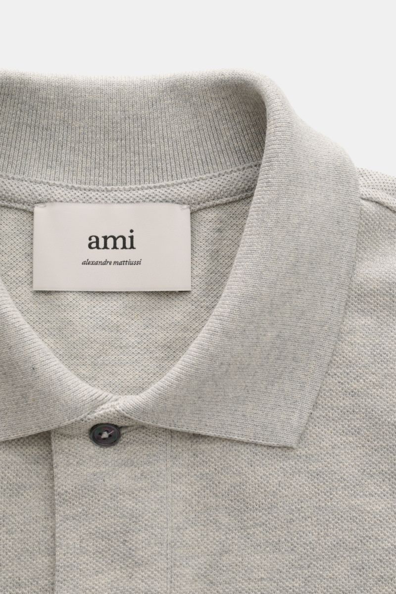 A close-up front view of the Ami Paris Poloshirt grau meliert showing the grey melange fabric, typical polo collar, and one visible button. Ein schöner Klassiker unter den Poloshirts: Das ikonisches Piqué-Modell aus reiner Bio-Baumwolle mit dem 'A'-Sti