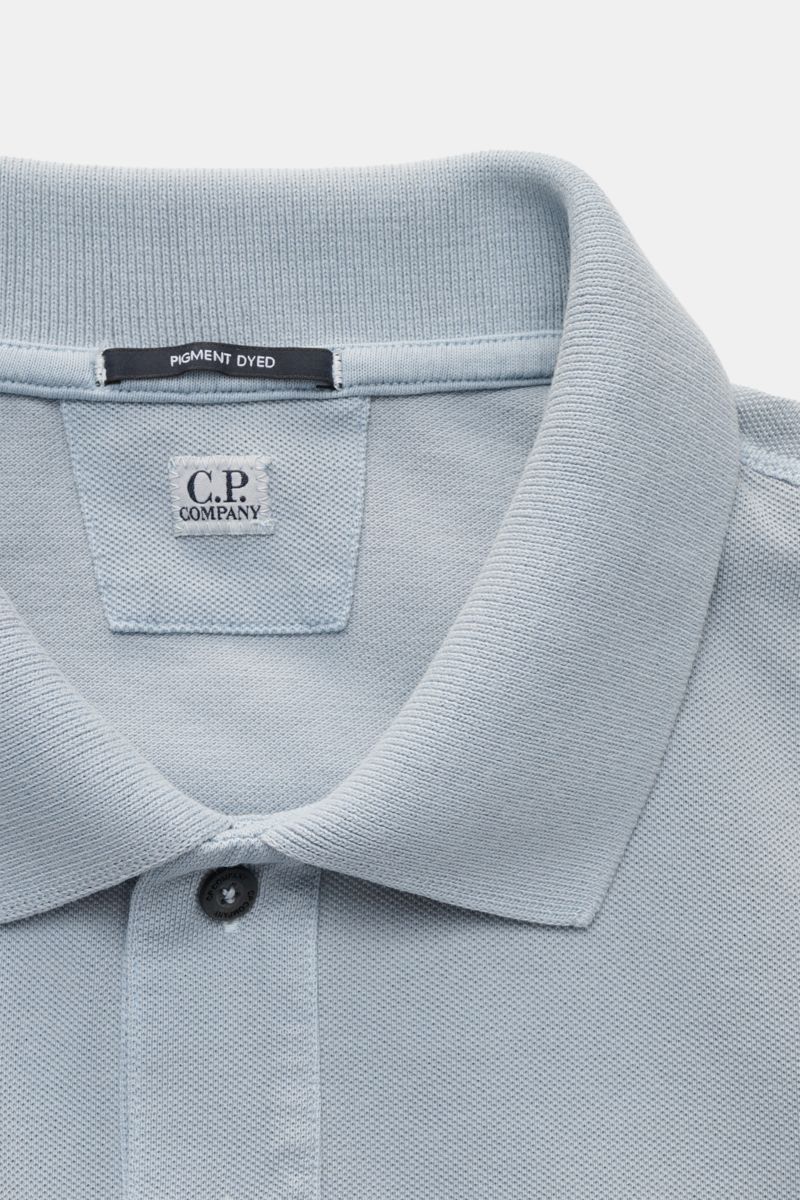 C.P. Company Poloshirt rauchblau, Nahaufnahme von Kragen, zwei Knöpfen, Weblabel und weichem Baumwoll-Piqué mit Pigment-Dye-Färbung.