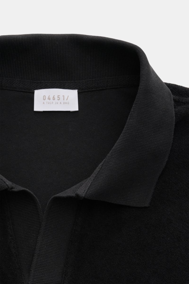 Schwarz fotografierte Nahaufnahme aus schräger Frontperspektive des 04651/ A trip in a bag Frottee-Poloshirt 'Terry Johnny' mit Polokragen, offener Kragenleiste, weichem Baumwoll-Frottee und kleinem Weblabel in der Seitennaht.