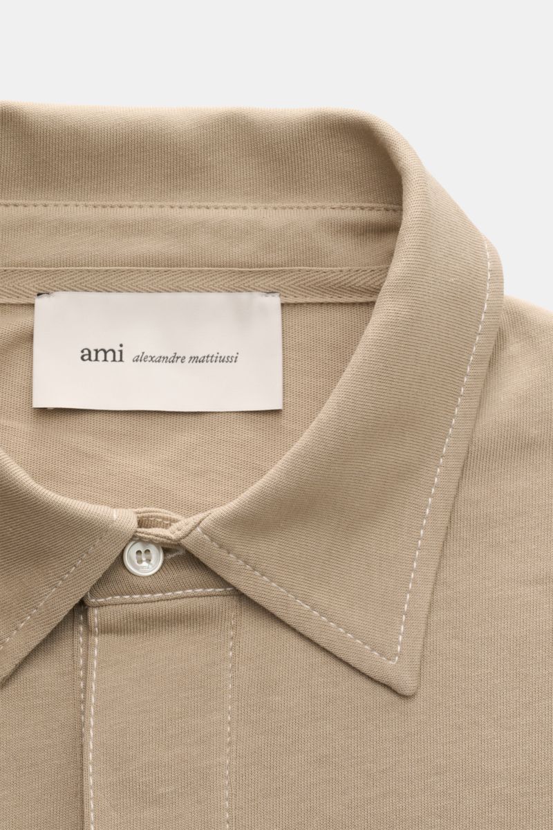 Close-up front view of the Ami Paris Jersey long sleeve polo shirt taupe, showing the dress-shirt collar, three-button patch placket, and signature logo stitching. Contemporary and casual: With its generous oversized fit, this long sleeve polo shirt by AM