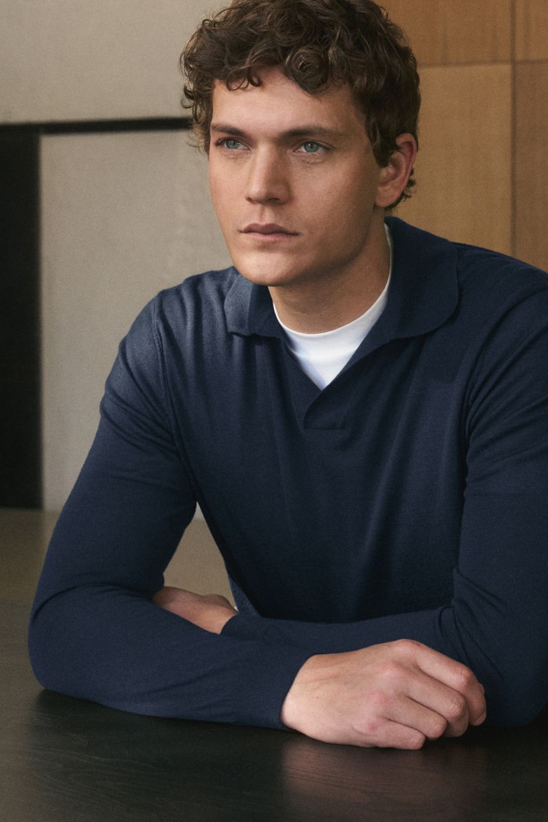 Mann von schräg vorne sitzend, trägt von Braun Merino Strickpolo navy aus reiner Merinowolle, offener Kragen, Regular Fit, elastische Rippbündchen.