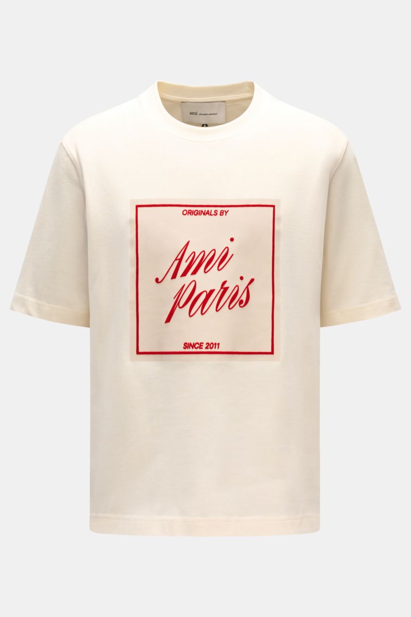 Ami Paris Rundhals-T-Shirt creme, frontal fotografiert, aus reiner Baumwolle, Regular Fit, weicher Griff, geflockter roter AMI PARIS-Schriftzug, Rundhalsausschnitt.