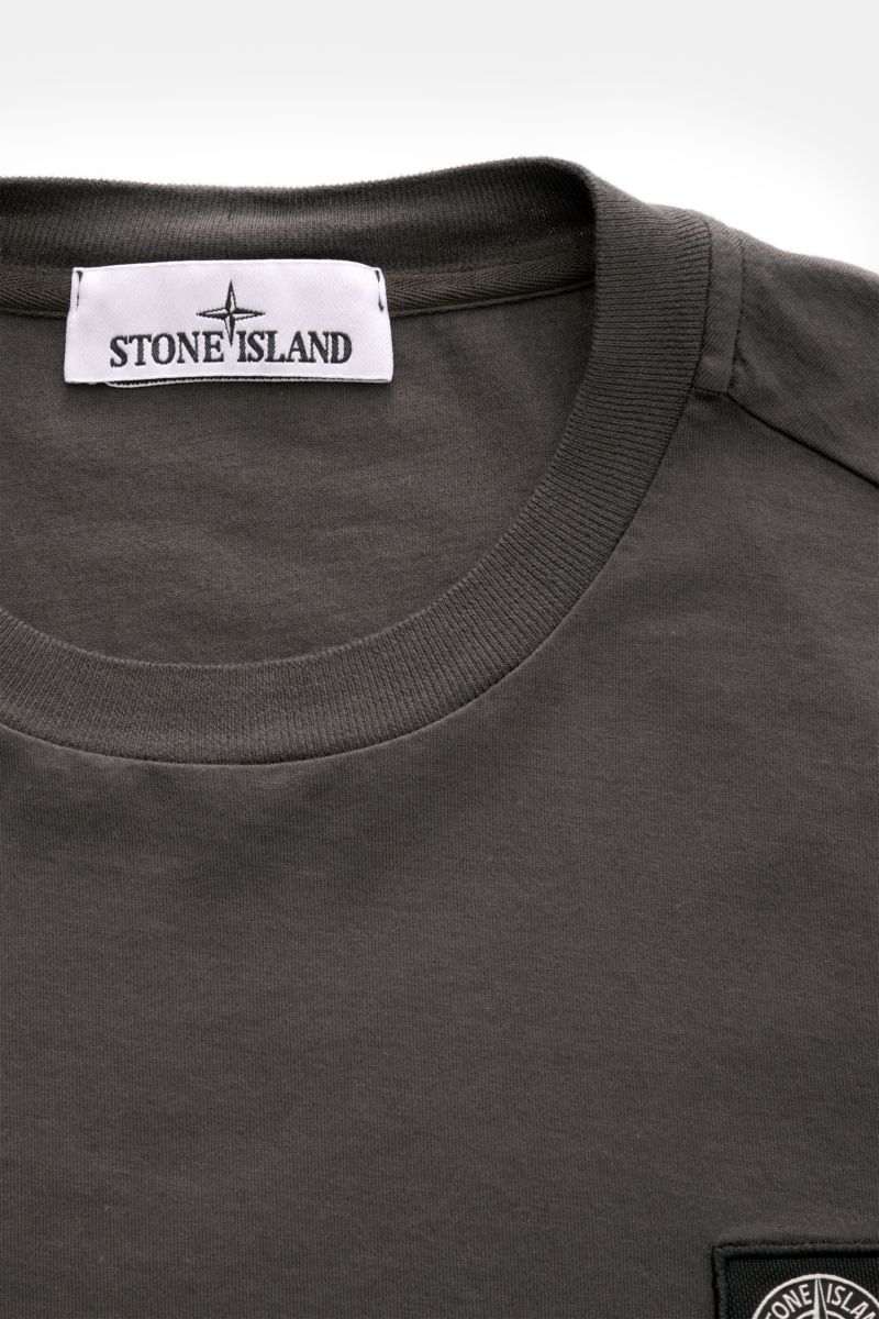 Close-up front top view of Stone Island Rundhals-Longsleeve 'Basic Cotton' dunkelgrau, a slim fit dark gray long sleeve with round neckline, soft cotton fabric, ribbed cuffs, and a Stone Island web label on the chest. Zeitloses Basic Piece: Das Longsle
