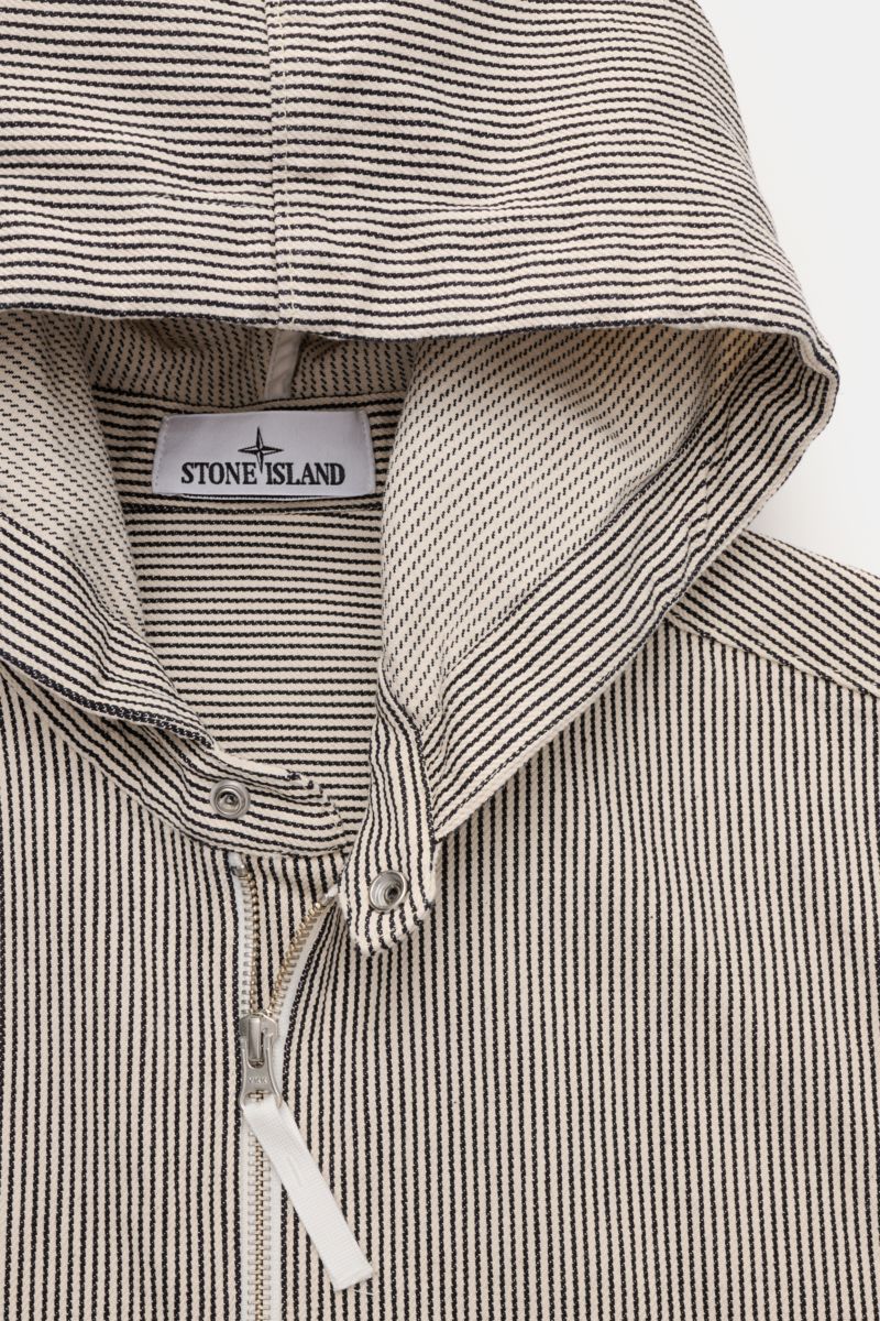 Close-up front view of the Stone Island Jacke 'Marina' navy/beige gestreift, showing navy and beige stripes, hood with drawstring, robust two-way zipper, and Stone Island label inside. Leichte Outerwear mit maritimem Charakter: Die Jacke aus der STONE ISL