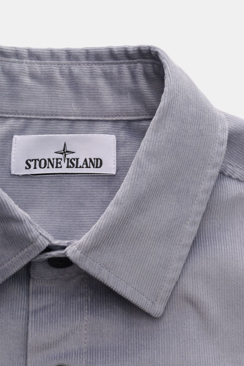 Nahaufnahme des Stone Island Cord Overshirts rauchblau von oben, zeigt Umlegekragen, weichen Bio-Baumwoll-Cord und Markenlabel innen.