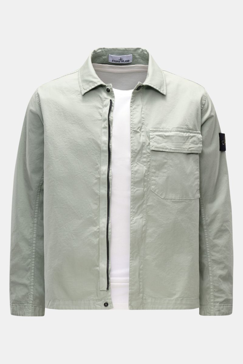 Front view of Stone Island Overshirt 'Stretch Cotton' salbei in light sage green, featuring soft, elastic cotton, slim fit, two-way zipper, snap buttons, turn-down collar, chest pocket with flap, signature compass badge on sleeve, and adjustable snap butt