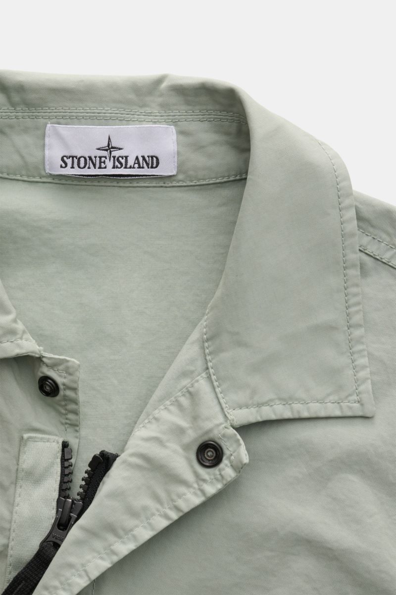 Close-up front top view of Stone Island Overshirt 'Stretch Cotton' salbei in soft sage green, showing elastic cotton fabric, slim fit, collar, zipper, and snap button details.

Description: Sportives Overshirt mit urbaner Lässigkeit: Dieser markante Hy