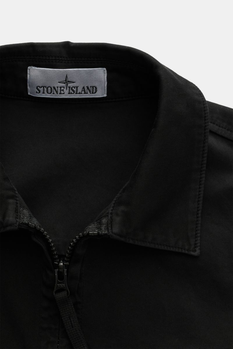 Close-up front view of the collar and zipper of the Stone Island Overshirt 'Cotton Satin' schwarz, featuring elastic cotton, soft touch, slim fit, two-way zipper, turn-down collar, chest pocket, compass badge on the upper arm, and buttoned sleeve cuffs. V