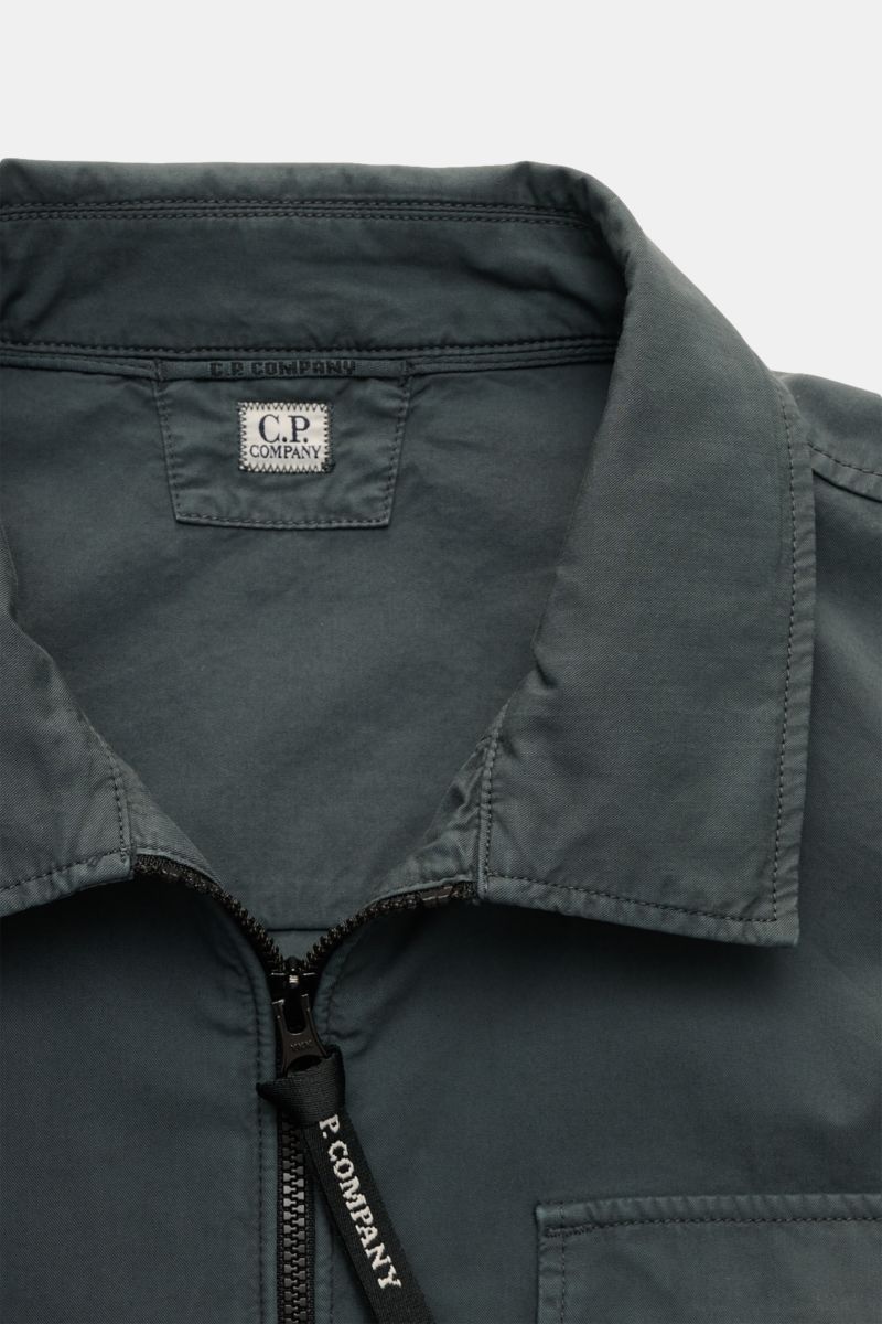 Nahaufnahme aus frontaler Perspektive des C.P. Company Overshirt dunkelgrau mit Umlegekragen, Zwei-Wege-Reißverschluss, Brusttasche, Manschetten und Logodetail am Ärmel.