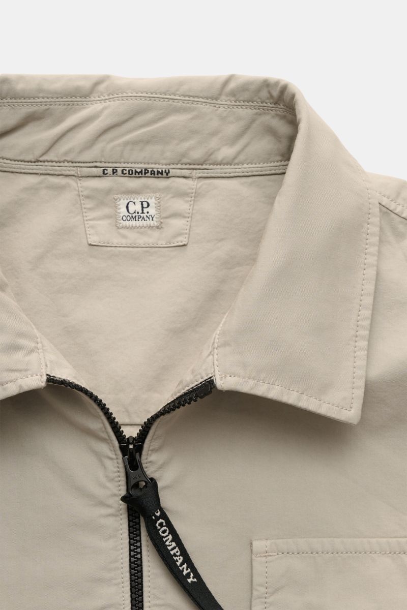 Nahaufnahme des C.P. Company Overshirt sand mit Umlegekragen, zwei-Wege-Reißverschluss, Brusttasche und Logodetail am Ärmel, reine Baumwolle.