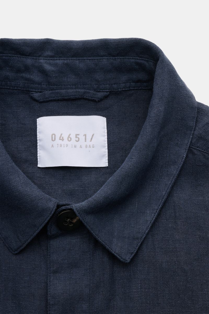 Nahaufnahme aus frontaler Perspektive des Kragens und des weißen Markenlabels des 04651/ A trip in a bag Overshirt 'Linen Jacket' navy aus weichem, reinem Leinen mit Slim Fit.