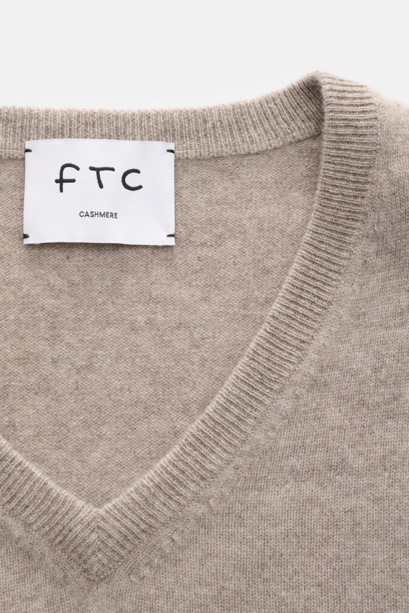 Nahaufnahme aus schräger Draufsicht eines taupefarbenen FTC Cashmere V-Neck Pullovers mit feinem Strickbild, V-Ausschnitt und Rippbündchen.