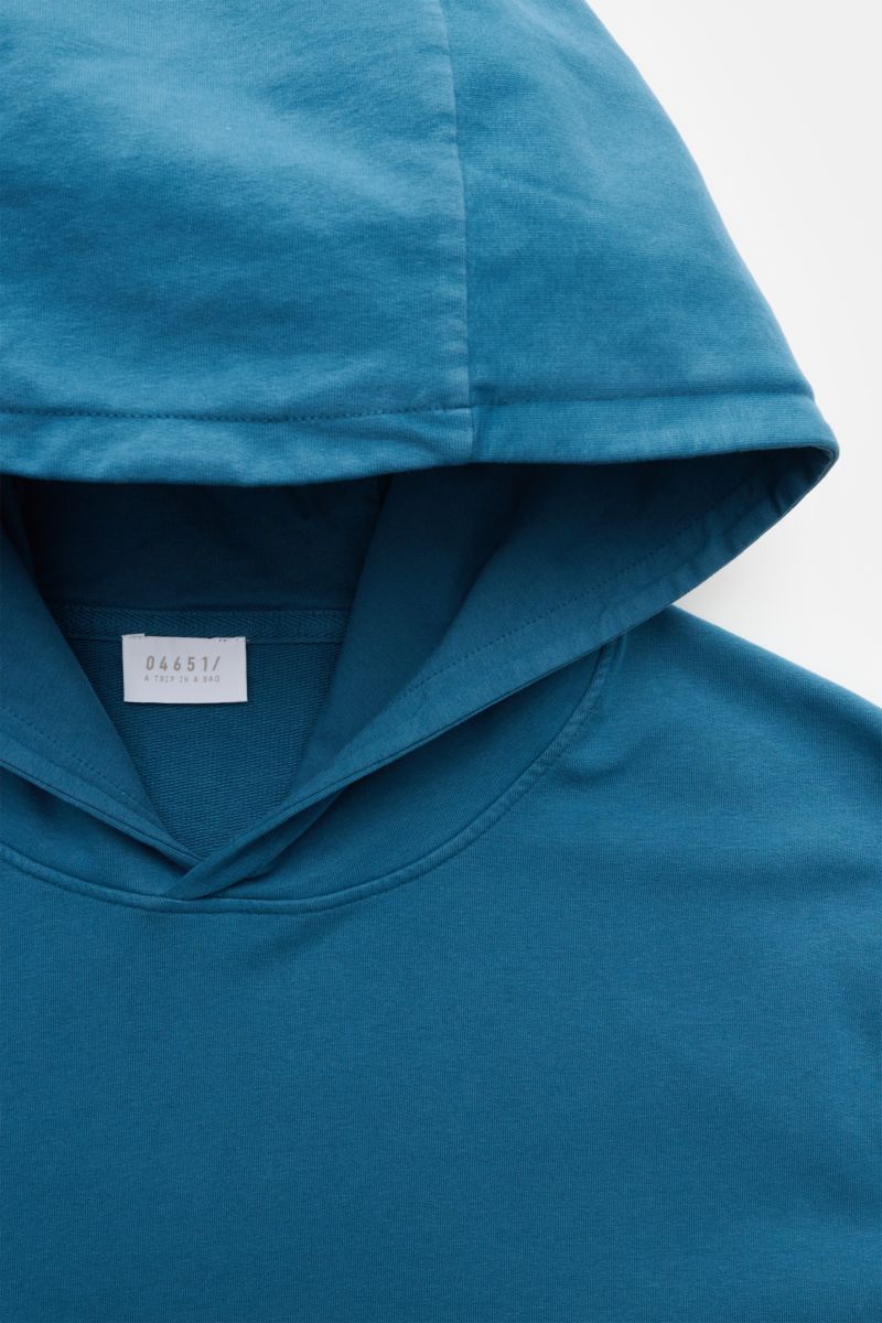 Close-up front view of the teal 04651/ A trip in a bag Hooded jumper 'IF Hoodie,' showing the practical hood, soft brushed jersey cotton, and label inside.