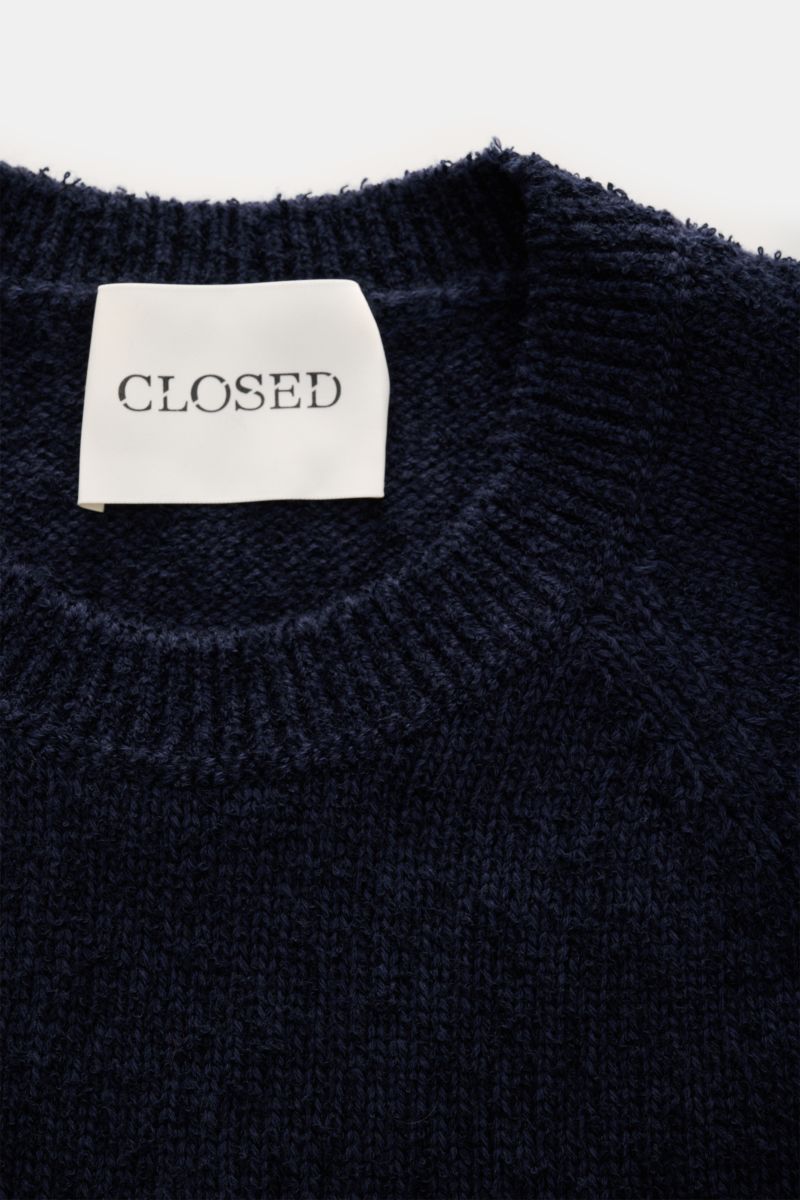 Close-up front view of a dark knit garment with a white 'CLOSED' label inside the collar; not the Closed Rundhals-Sweatshirt hellgrau meliert.

Description: Dieser relaxte Sweatshirt aus reiner Baumwolle vom Hamburger Label CLOSED ist mit seinem gummie