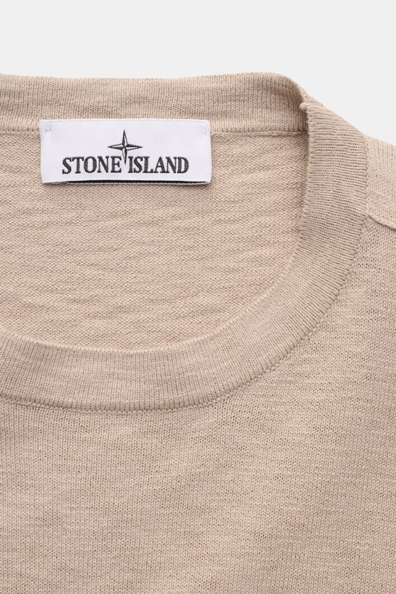Nahaufnahme des Stone Island Rundhalspullover beige von oben, mittelfeines Strickbild, weicher Griff, Slim Fit, Rundhalsausschnitt, Kompass-Badge am Oberarm.