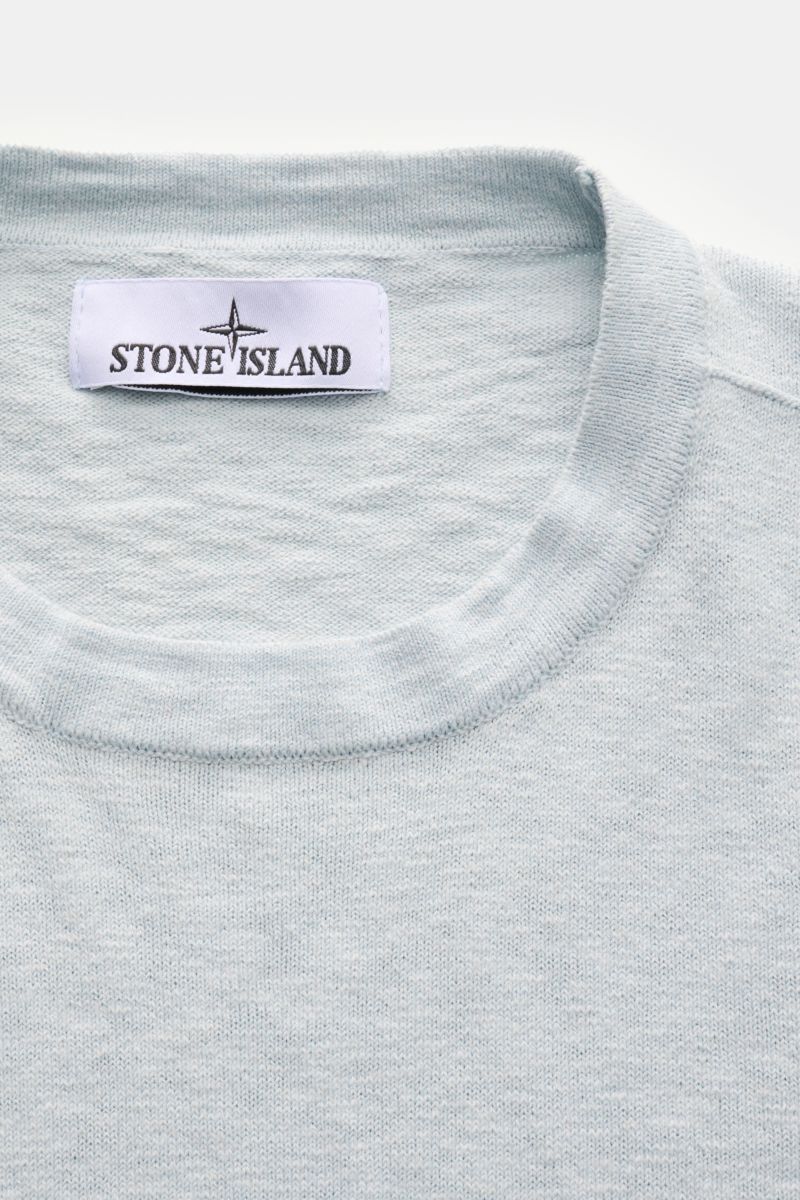 Nahaufnahme des Stone Island Rundhalspullover pastellblau von oben, mit feinem Strickbild, rolliertem Saum und Kompass-Badge.