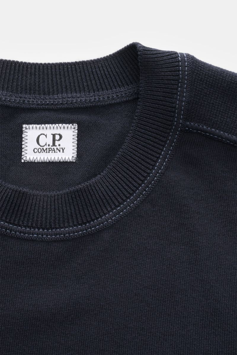 Close-up front top view of the C.P. Company Crew neck jumper navy, showing ribbed crew neckline, fine knit texture, and white brand label sewn inside the collar. 