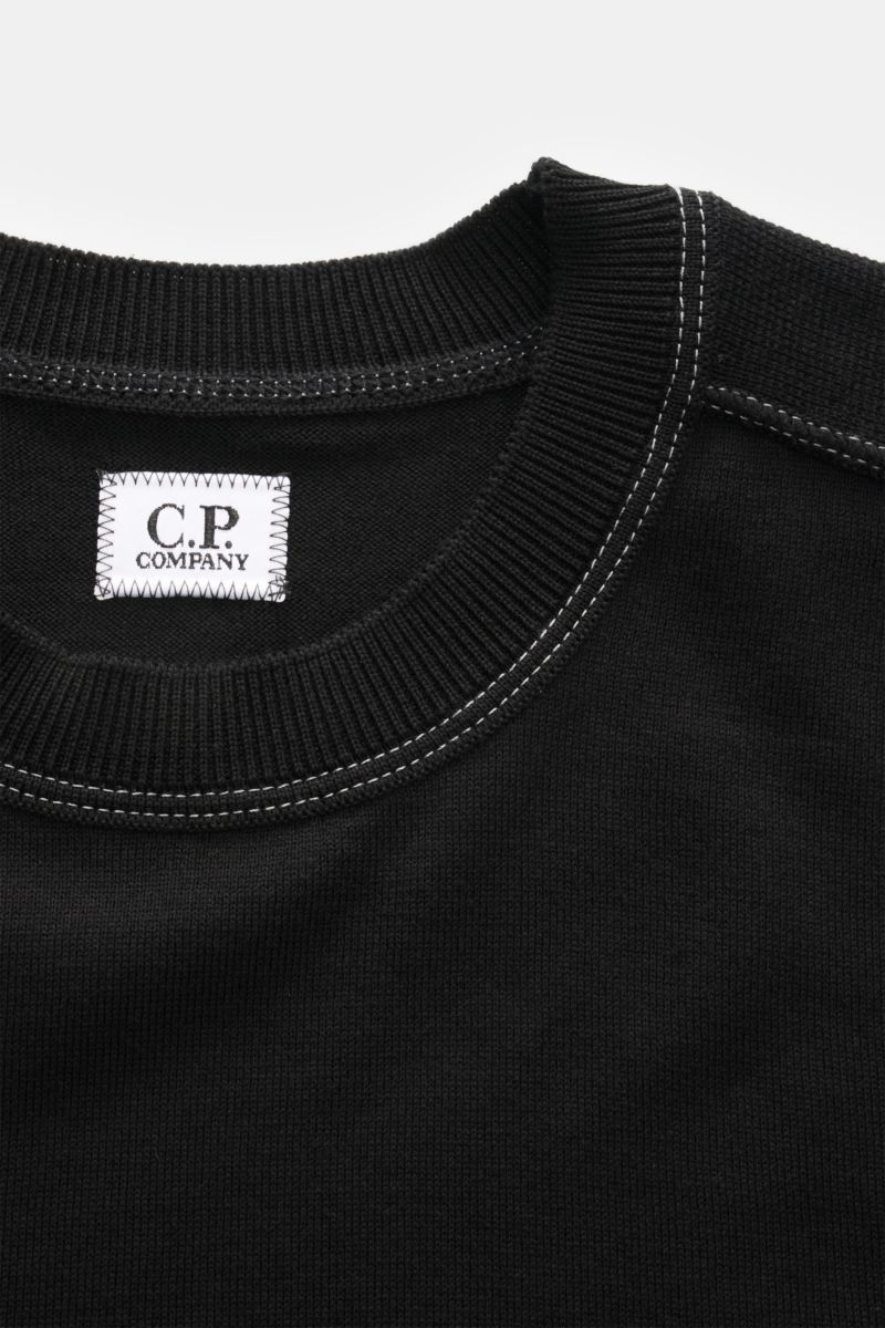 Close-up top-down view of the ribbed crew neck and label of the C.P. Company Crew neck jumper black, showing fine knit and contrasting white stitching. 