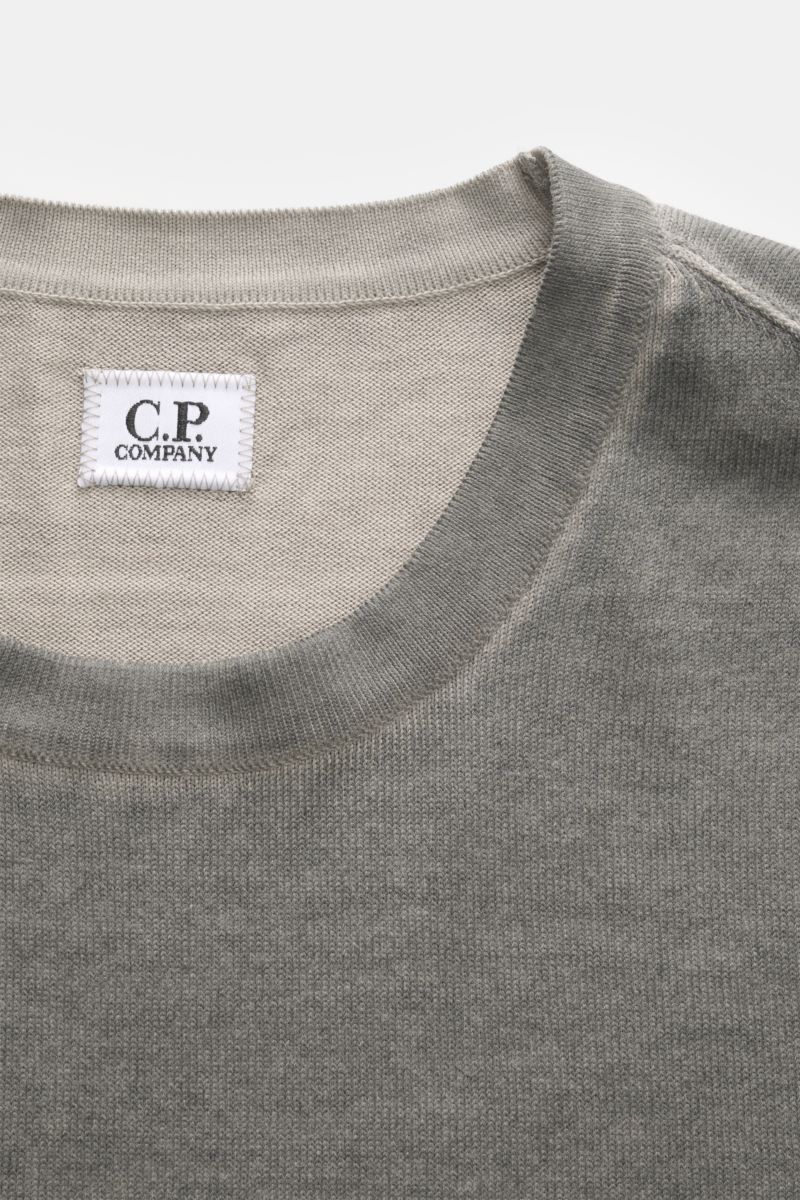 C.P. Company Crew neck jumper grey shown from a top-front close-up, featuring soft pure cotton, garment-dyed design, fine knit, regular fit, ribbed bands, and a logo print on the sleeve hem.

With its distinctive garment-dyed design, this crew neck jum