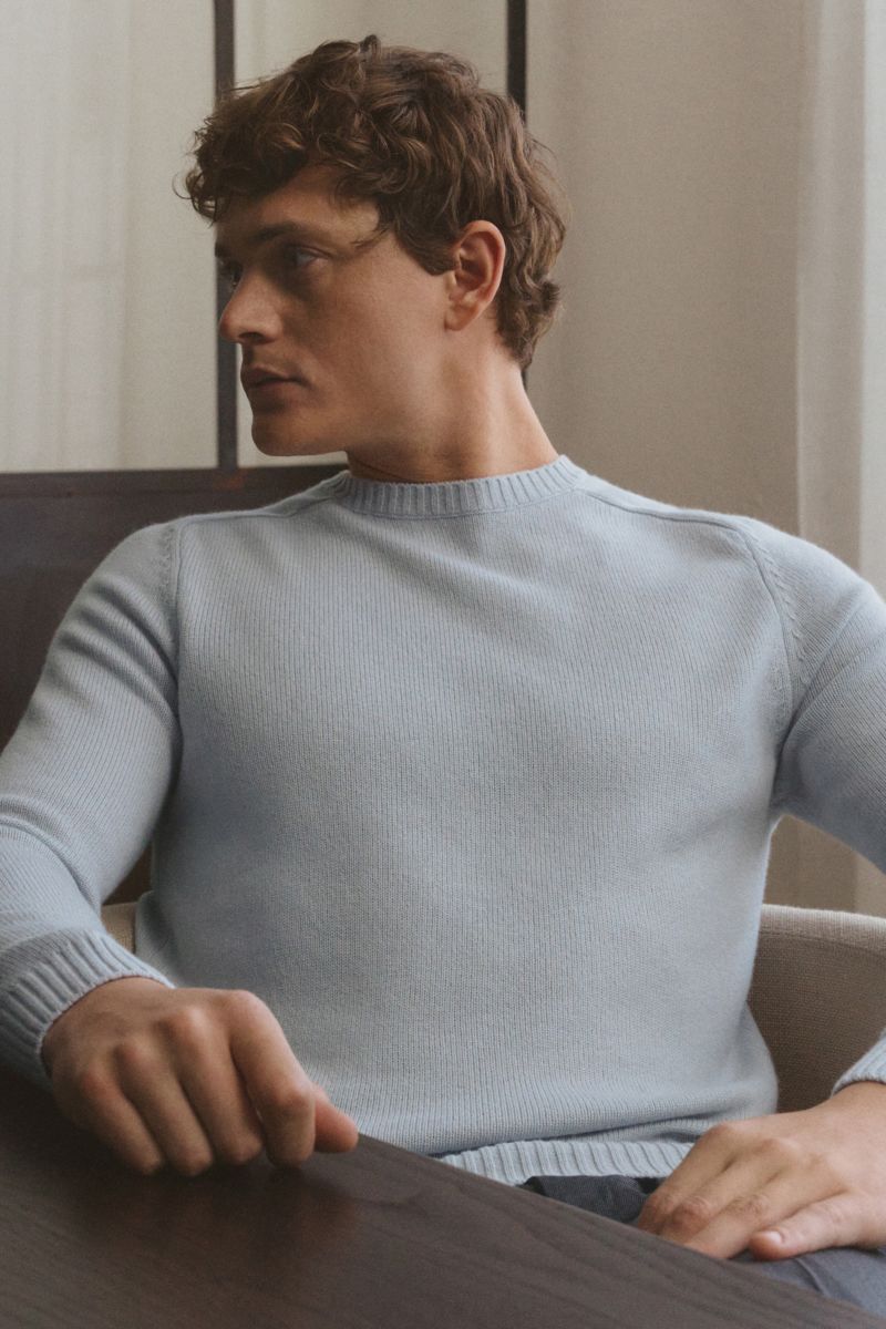 Junger Mann frontal sitzend in von Braun Cashmere Rundhalspullover hellblau, slim fit, mittelfeines Strickbild, weicher Griff, Rundhalsausschnitt, elastische Rippbündchen.