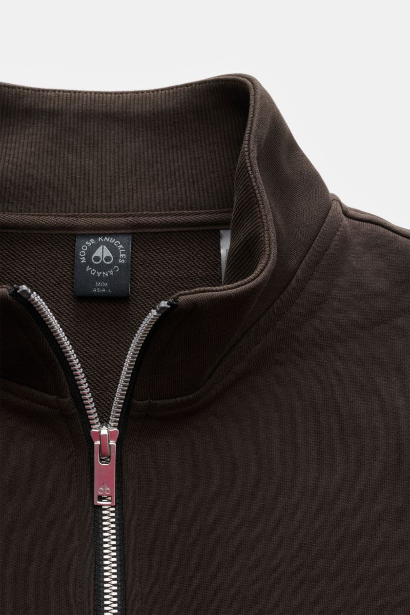Close-up front view of the Moose Knuckles Sweat-Troyer 'Hartsfield' graubraun, showing hoch schließender Kragen mit Zipper, Sweat aus reiner Baumwolle, weicher Griff, Regular Fit, typisches Metall-Logo am Oberarm, and elastische Rippbündchen.