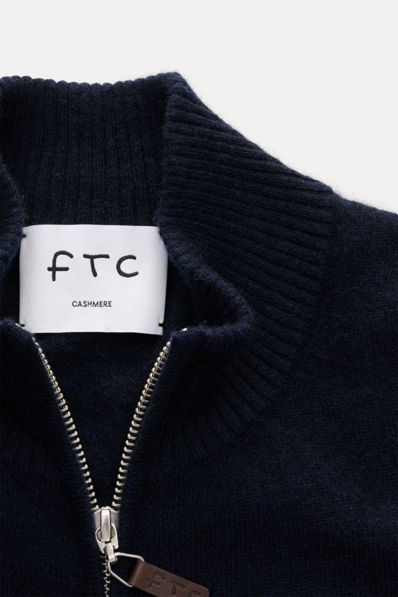 Close-up front view of the navy FTC Cashmere cardigan showing ribbed standing collar, fine knit texture, concealed two-way zip with leather embossed logo pull, and inside label. 

Fair Trade cashmere, timeless design: This cardigan by FTC has been sust
