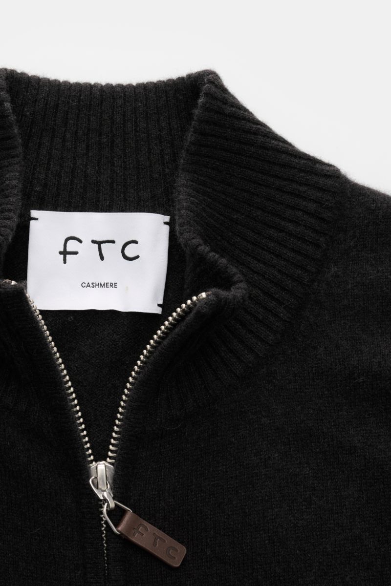 Close-up front view of FTC Cashmere cardigan dark brown showing ribbed standing collar, concealed two-way zip with leather FTC logo detail, and fine knit texture.

Fair Trade cashmere, timeless design: This cardigan by FTC has been sustainably produced
