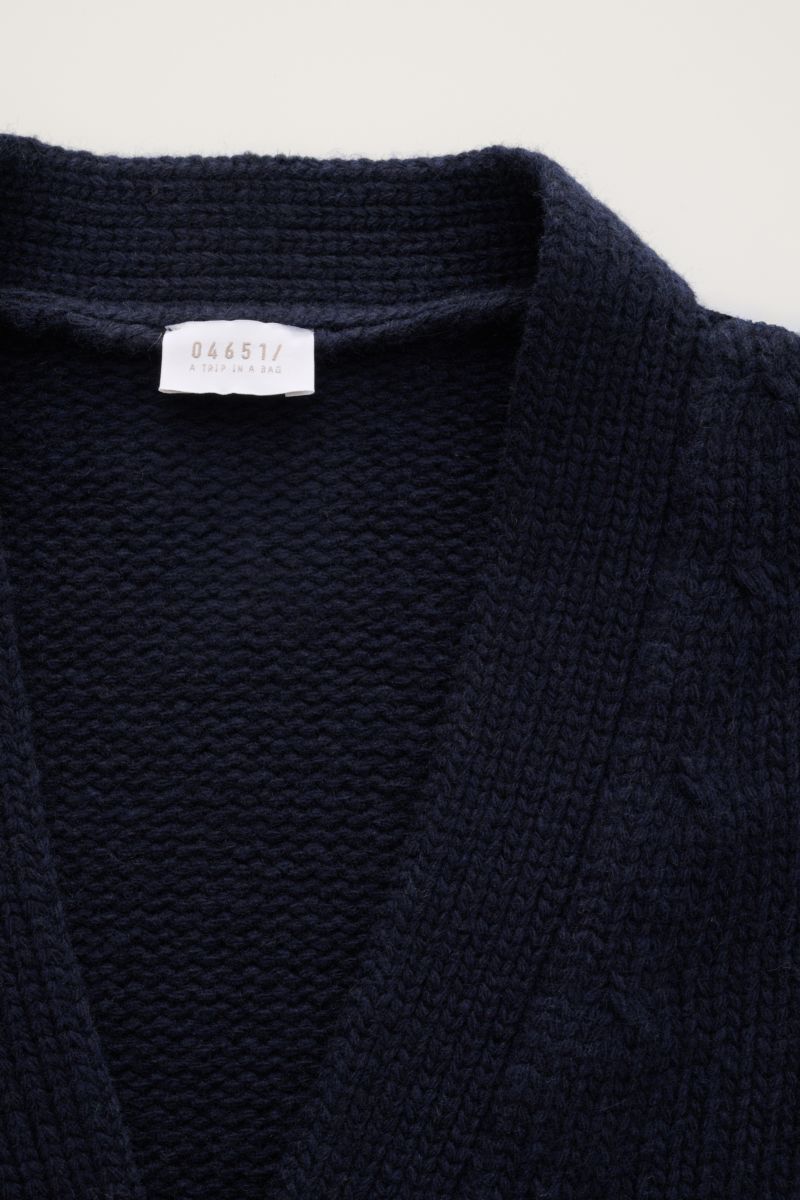 Nahaufnahme des dunkelblauen 04651/ A trip in a bag Cardigan 'Bold' navy aus reiner Lammwolle, grobes Strickbild, weicher Griff, Oversized Fit, mit Label innen am Kragen, fotografiert von oben.