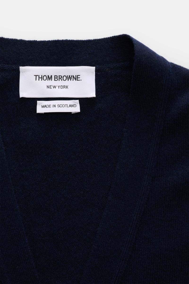 Close-up top-front view of Thom Browne Cashmere Cardigan navy showing white brand label and deep V-neck collar in soft, fine-knit pure cashmere fabric. Vielseitiger Style-Favorit: Der Cashmere Cardigan von THOM BROWNE kombiniert luxuriöse Materialien mit 