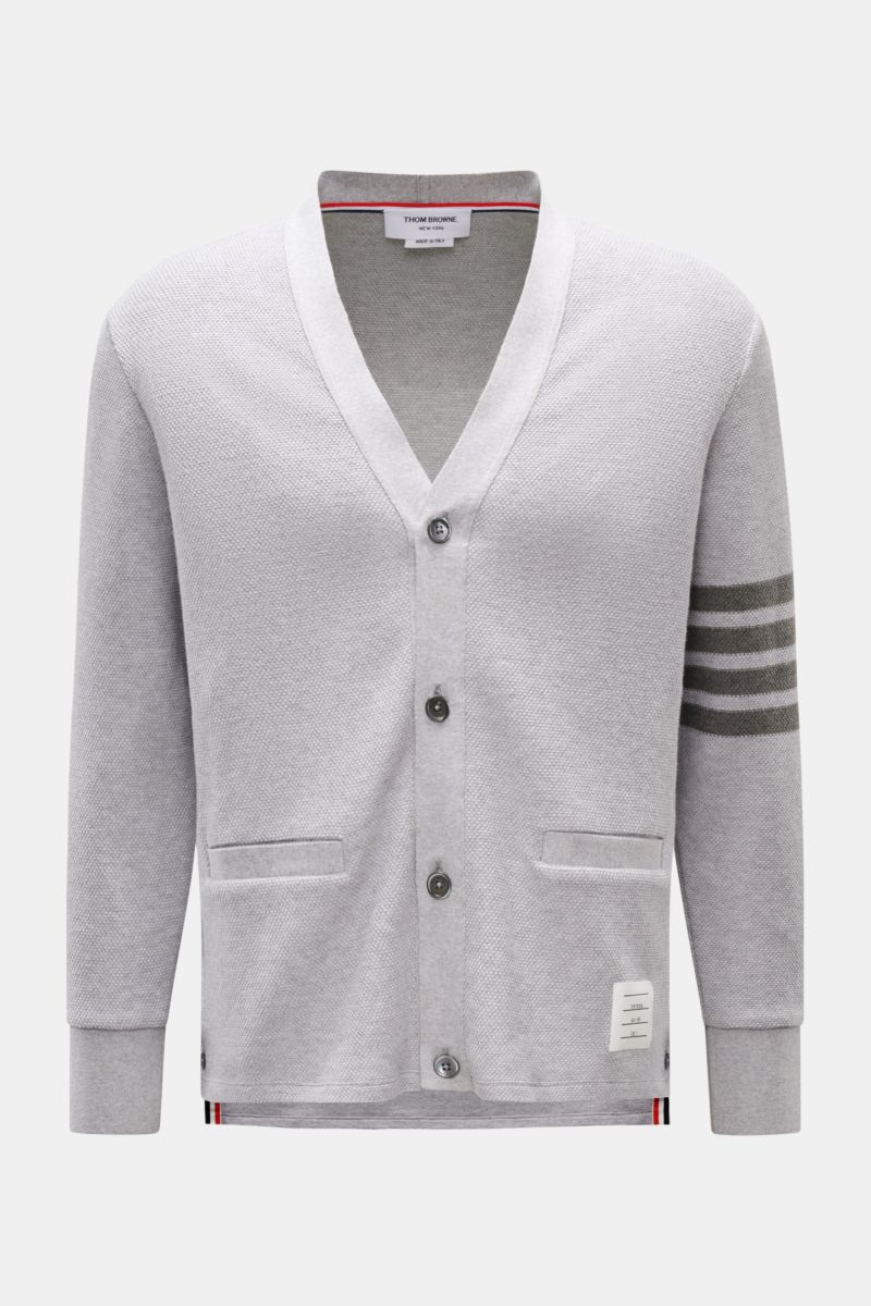 Front view of Thom Browne Cardigan light grey mottled with pure cotton, V-neck, dark mother-of-pearl buttons, tricolour ribbed band, hip pockets, and contrasting sleeve stripes.