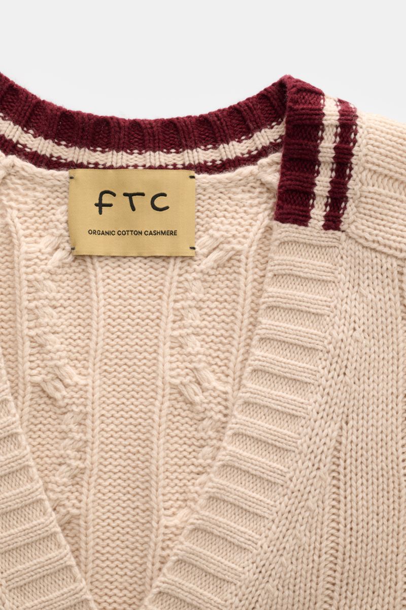 Nahaufnahme des FTC Cardigan beige mit Zopfstrick-Design, V-Ausschnitt, breiten Kontrastkanten und Label, nachhaltig aus Bio-Baumwolle und Fair-Trade-Cashmere.